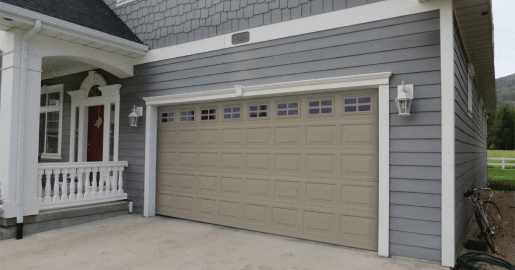 Taupe garage door with windows on gray house.
